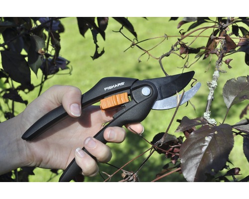 Ruka stříhá větev zahradními nůžkami značky Fiskars