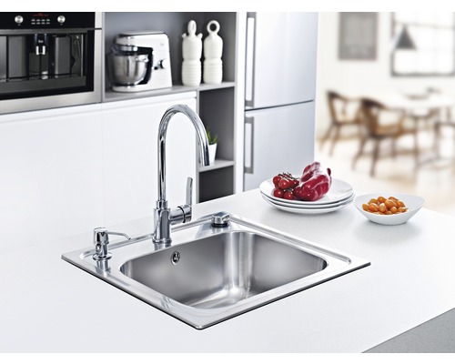 Nerezový kuchyňský dřez s baterií a dávkovačem saponátu ve světlé kuchyni.