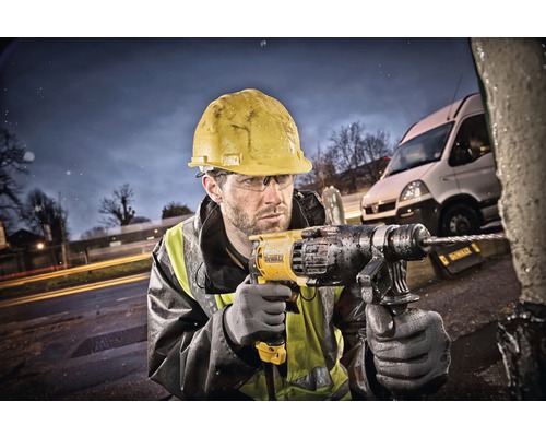 Stavební dělník s ochrannou helmou vrtá vrtačkou do objektu venku.