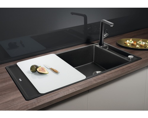 Černý kuchyňský dřez s baterií, prkénkem, fíky a nožem.