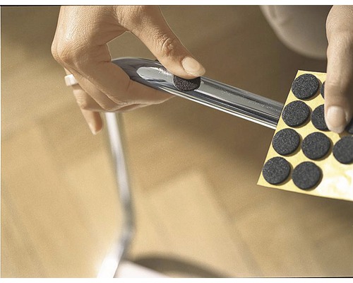 Osoba připevňuje plstěný kluzák k noze židle pro ochranu podlahy.