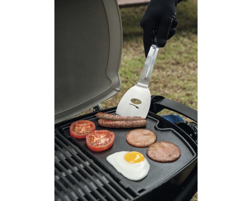 Gril s klobásami, rajčaty, slaninou a smaženým vejcem a osobou s obracečkou