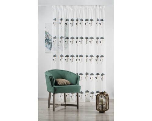 Dekorativní obývací pokoj se zeleným křeslem, lucernou a bílým závěsem s květinovým vzorem.