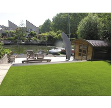 Umělý trávník v zahradě u vody se zahradním domkem a posezením.