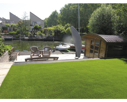 Umělý trávník v zahradě u vody se zahradním domkem a posezením.