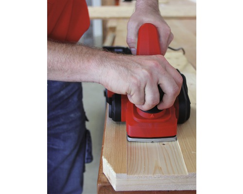 Osoba hobluje dřevěnou desku elektrickým hoblíkem.