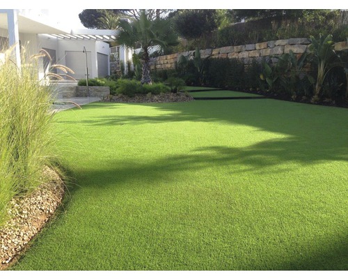 Zelený umělý trávník na zahradě s rostlinami