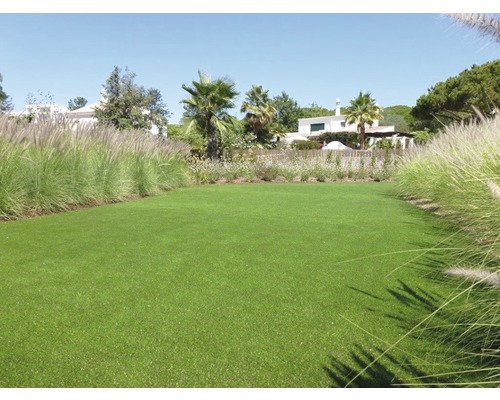 Plocha umělého trávníku v zahradě s rostlinami a obytnými domy v pozadí.