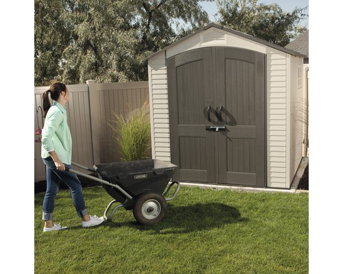 Žena tlačí kolečko před zahradním domkem.