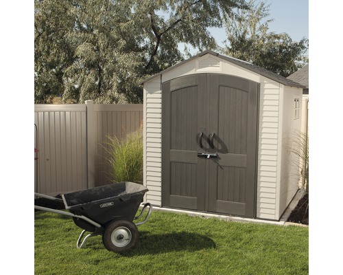 Zahradní scéna s kůlnou a kolečkem na trávníku.