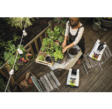 Žena přesazuje rostliny na dřevěné terase s půdou, obklopená zahradním nářadím a dekoracemi