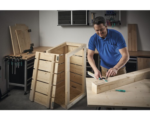 Muž staví dřevěnou bednu v dílně.