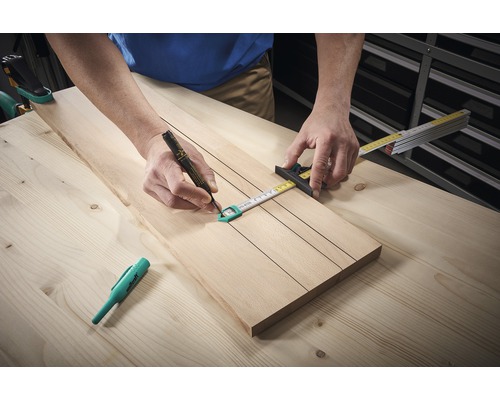 Osoba kreslí tužkou čáry na dřevěnou desku pomocí svinovacího metru.