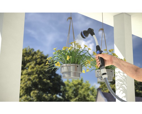 Osoba zavlažuje závěsné květináče zahradní stříkací pistolí.