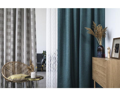 Dekorativní interiér s různými závěsy, ratanovým křeslem a dřevěnou skříňkou