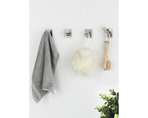 Tři nástěnné háčky s ručníkem, sprchovým míčem a kartáčem na zdi