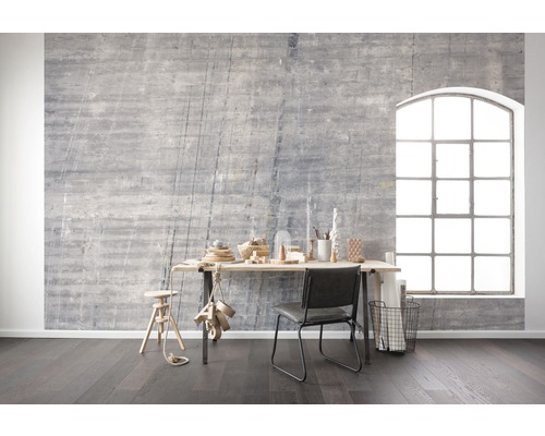 Obývací pokoj s šedou betonovou stěnou, psacím stolem, židlí a velkým oknem pro světlou a moderní atmosféru.