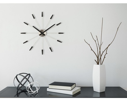 Dekorativní scéna s nástěnnými hodinami, vázou, větvemi, knihami a ozdobnými koulemi na stole.