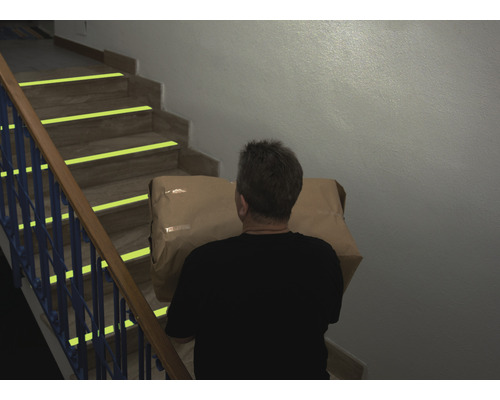 Osoba nese balík po schodech se značkami bezpečnosti.