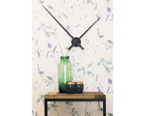 Dekorace s nástěnnými hodinami, skleněnou vázou a svíčkami na dřevěném stole před květinovou tapetou