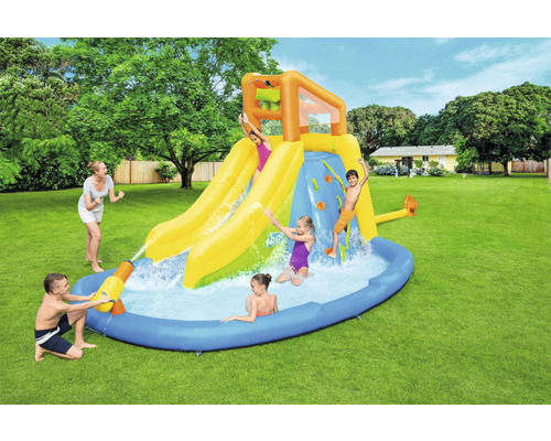 Nafukovací aquapark se skluzavkami, horolezeckou stěnou a brouzdalištěm na zahradě s hrajícími si dětmi.