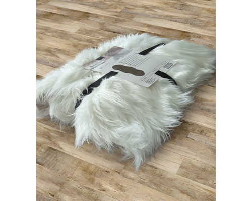 Bílý koberec z umělé kožešiny, srolovaný a označený etiketou na dřevěné podlaze