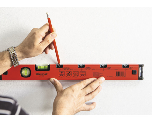 Osoba značí tužkou místo na stěně pomocí vodováhy.