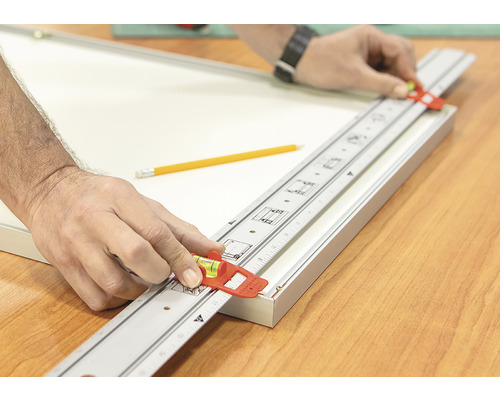 Řemeslník používá měřicí tyč s vodováhou k vyrovnání rámu obrazu.