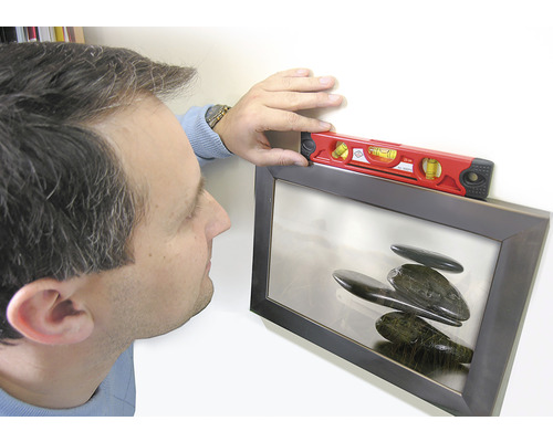 Osoba vyrovnává zarámovaný obraz pomocí vodováhy.