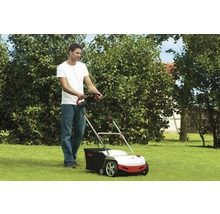 Muž používá vertikutátor na zahradě.