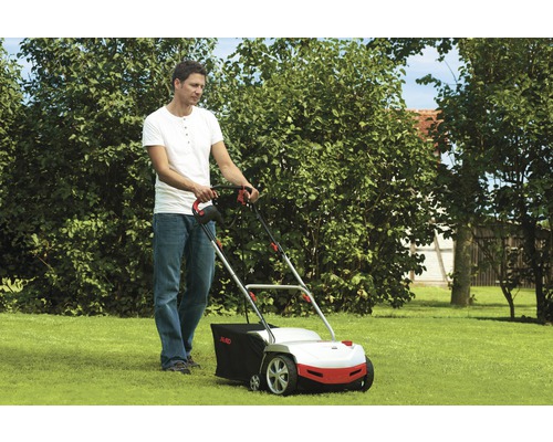 Muž používá vertikutátor na zahradě.