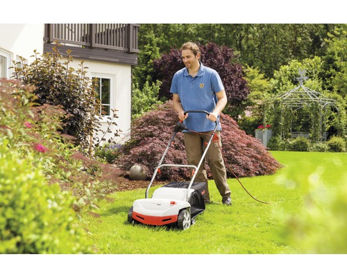 Muž používá sekačku na trávu na zahradě.