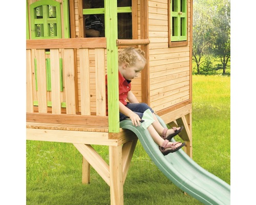 Dítě na skluzavce dřevěného hracího domku na zahradě.