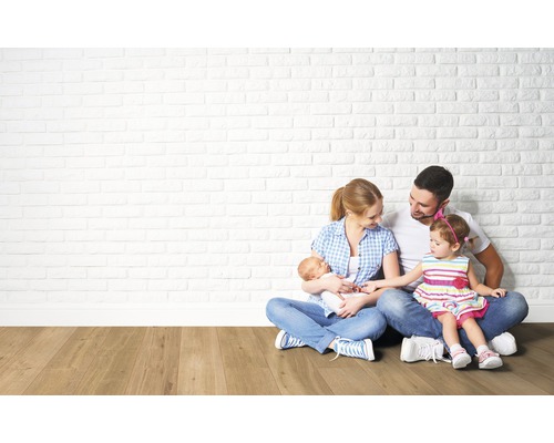 Rodina sedí na dřevěné podlaze před zdí z cihel.