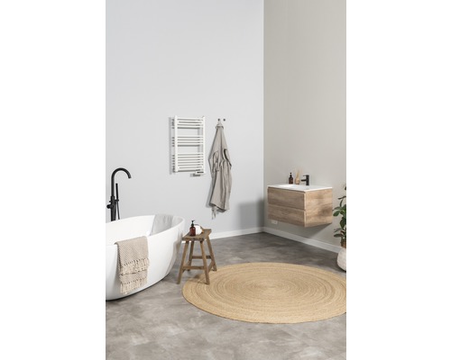 Světlá koupelna s volně stojící vanou, skříňkou pod umyvadlo, topným tělesem na ručníky a kulatým kobercem