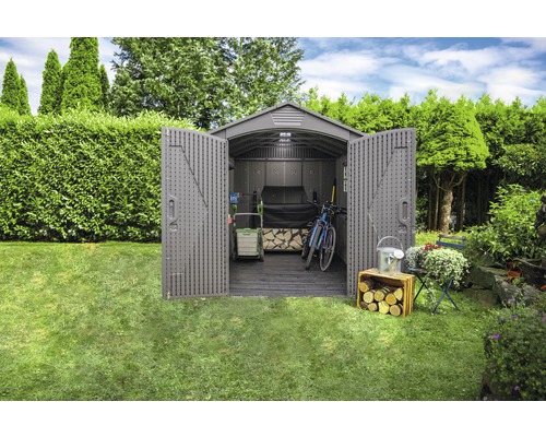 Zahrada s otevřenou kůlnou na nářadí s uloženým zahradním nářadím, jízdním kolem a dřevem.