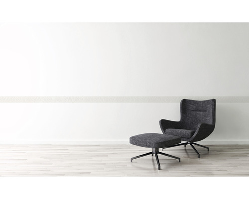 Moderní interiér s křeslem a podnožkou na světlé dřevěné podlaze před bílou stěnou