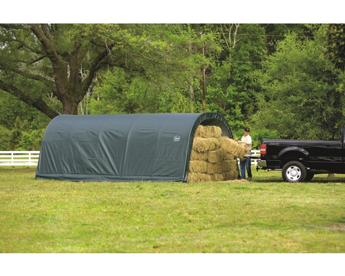 Šedá skladovací hala pro balíky sena na louce, osoba vykládající balík sena poblíž pickupu.
