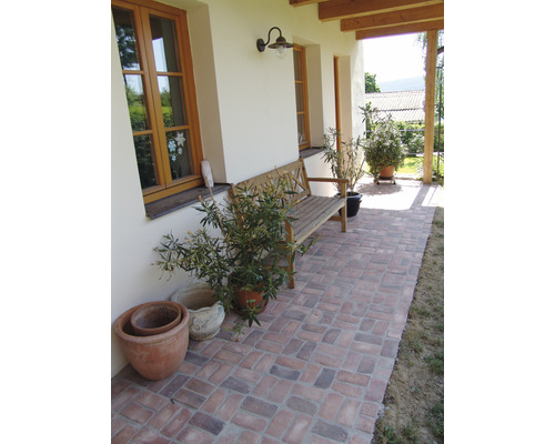 Krytá terasa s kamennou dlažbou, dřevěnou lavicí a hrnkovými rostlinami.