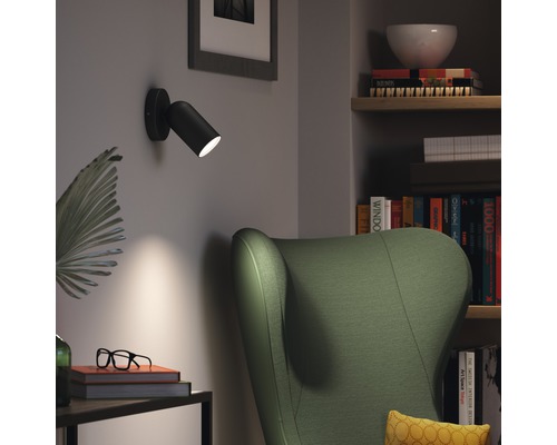 Obývací pokoj s křeslem, knihovnou a černým nástěnným svítidlem