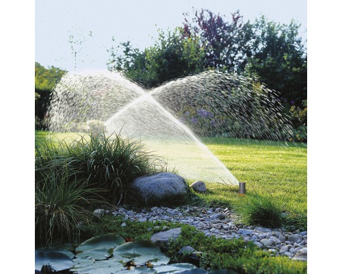 Zavlažování zahrady s travním postřikovačem v provozu na trávníku.