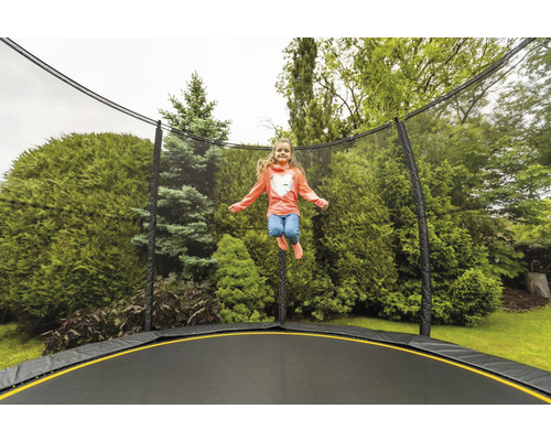 Dívka skáče na zahradní trampolíně s bezpečnostní sítí před stromy
