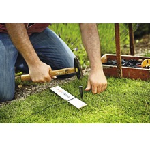 Osoba zatlouká kolík kladivem do země pro upevnění systému Gardena Micro-Drip.