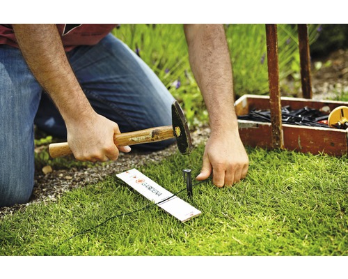 Osoba zatlouká držák trubky systému Gardena Micro-Drip do trávníku