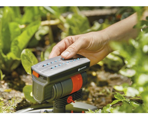 Ruka ovládá zavlažovač Gardena na zahradě.