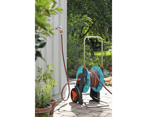 Zahradní scéna s vozíkem na zahradní hadice s připojením hadice na vodovodní kohoutek