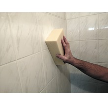 Ruka drží houbu na obkládané stěně.