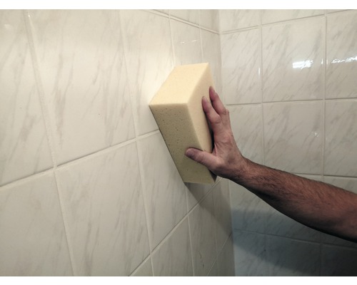 Ruka drží houbu na obkládané stěně.