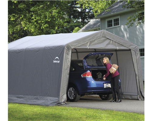 Šedá autodílna s autem a ženou vykládající kufr.