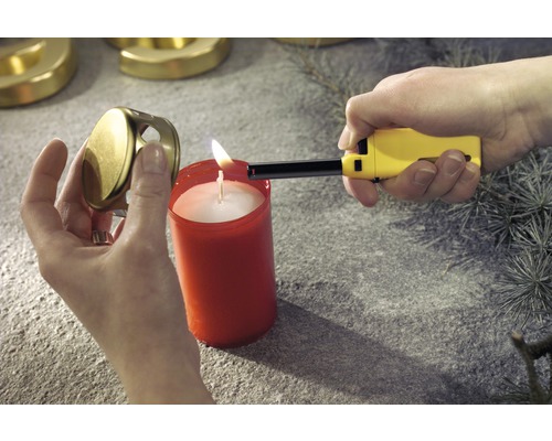 Osoba zapaluje svíčku zapalovačem. Vedle svíčky leží víčko na svíčku.